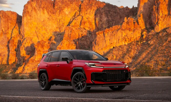 Front three-quarter view of a red 2026 Toyota RAV4 GR SPORT parked against a rocky desert landscape.
