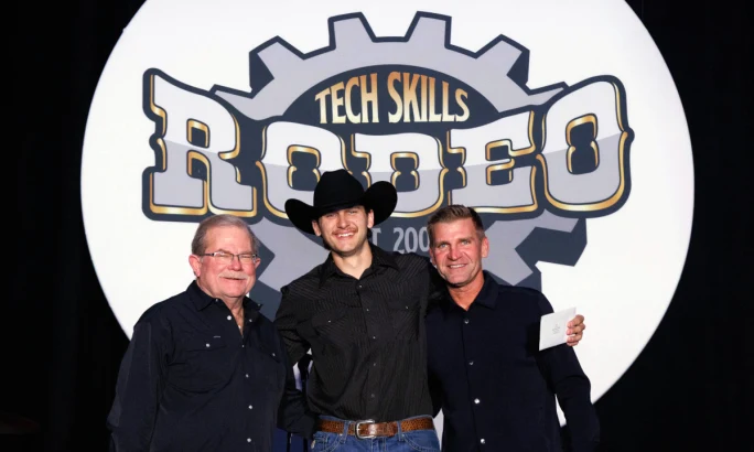 Young man in cowboy had stands between two men dressed in black in front of a Rush Tech Skills logo background.