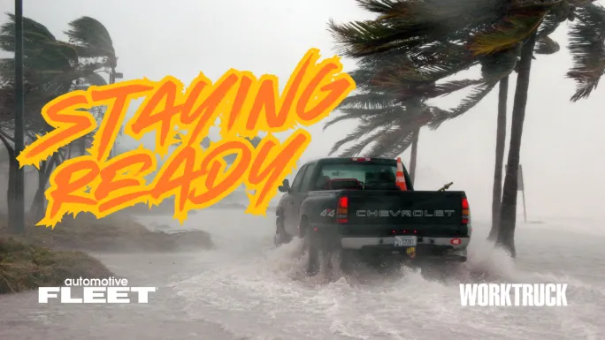 Pickup truck driving through flooded road during storm with strong winds and palm trees, showing fleet response in severe weather