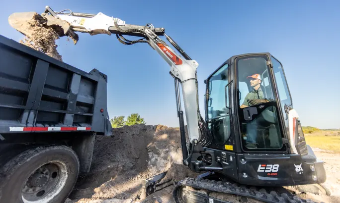 Bobcat excavator loading dirt into a dump truck.
