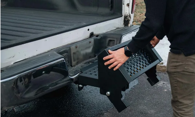 Man folding two steps up against the rear of a pickup truck.