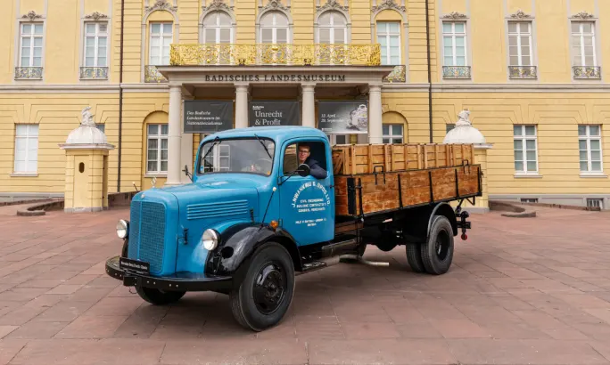 Blue vintage Mercedes-Benz flatbed truck parked in front of a historic museum building.