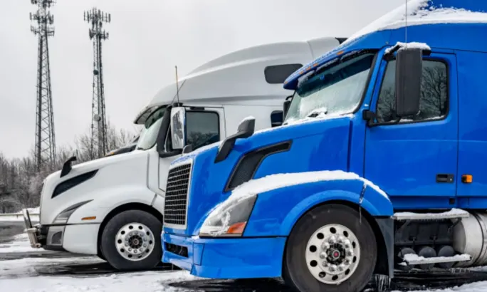 Two semi trucks parked in snowy lot, illustrating winter fleet maintenance challenges like weak batteries, air system issues, and tire pressure swings.