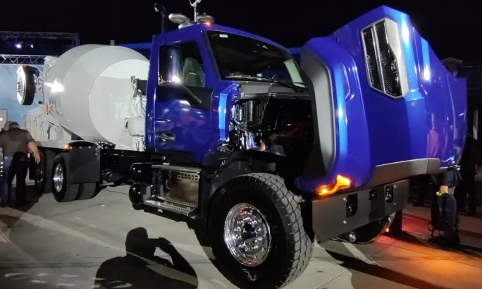 Blue concrete truck parked with the hood tipped open.