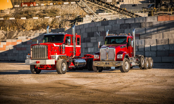 Angled view of two red Kenworth trucks parked on a job site.