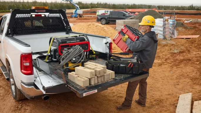 Worker using pull-out storage system in pickup truck bed to access tools and equipment at a jobsite.