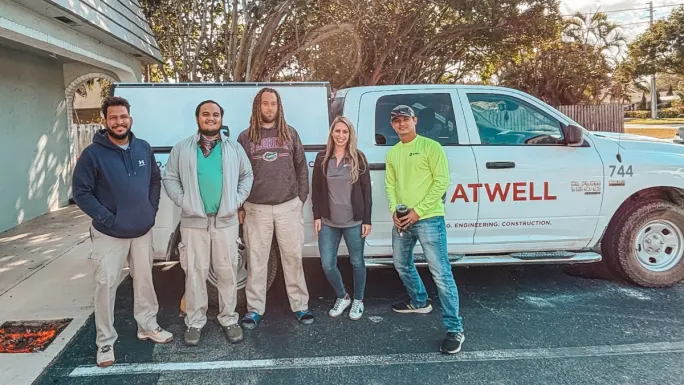 Small group of Atwell team members stand beside a branded work truck in a parking area, dressed in work attire.