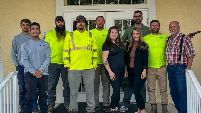 Group of Atwell employees pose together outside an office entrance, wearing a mix of work gear and casual clothing.