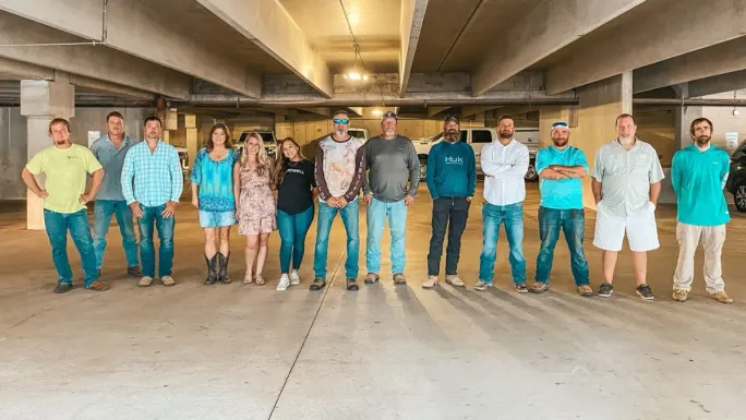A large group of Atwell employees stand together in a parking garage, lined up for a team photo.