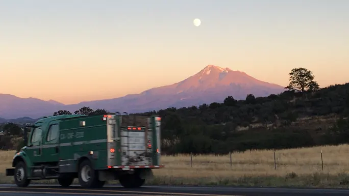 Green fire truck driving on road with mountain backdrop at sunset, symbolizing active disaster response deployment