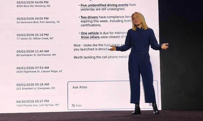 Woman presenting onstage beside a large screen displaying fleet management alerts, driver compliance updates, and maintenance notifications, with an “Ask Atlas” interface visible at the bottom.