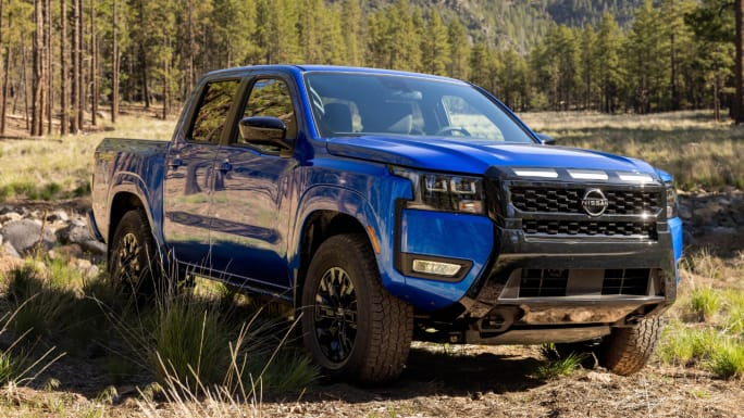 Blue 2027 Nissan Frontier pickup truck parked on a dirt trail in a forest setting, showcasing the midsize truck's capability and updated design.