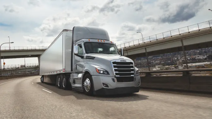 White Cascadia Freightliner truck driving down an empty highway.