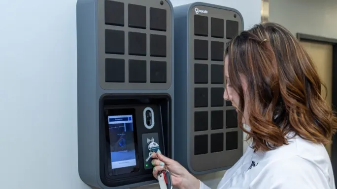 A woman holds a vehicle key fob to a Keycafe electronic key cabinet while accessing a stored fleet key.