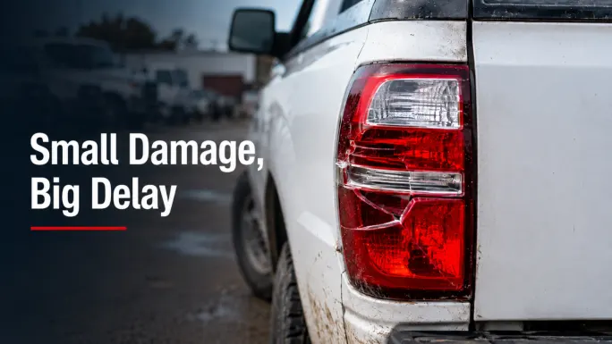 Close-up of a cracked red taillight on the rear of a white work pickup truck.