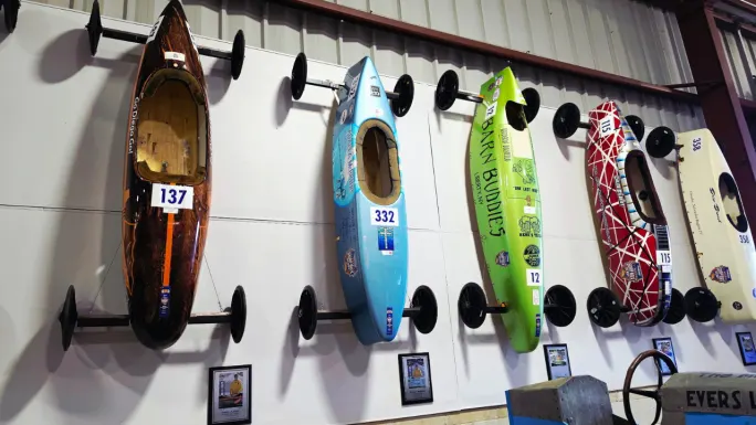 Historic Soap Box Derby race cars in different colors and designs displayed vertically inside the Derby museum in Akron, Ohio.
