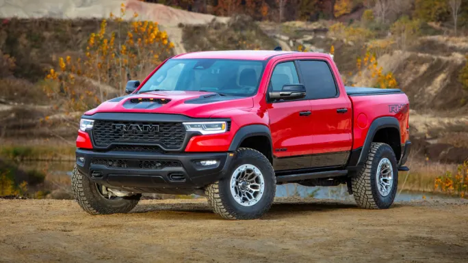 Red 2025 Ram 1500 RHO pickup parked on a dirt overlook with autumn trees in the background.