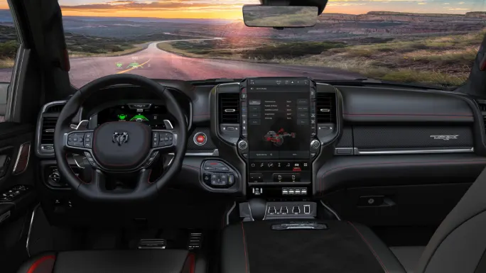 Interior of a Ram 1500 TRX showing the steering wheel, digital instrument cluster, large center touchscreen, head-up display, and black dashboard with red stitching.