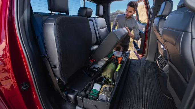 Man lifting the rear seat cushion inside a Ford F-150 to access under-seat storage holding tools and gear.