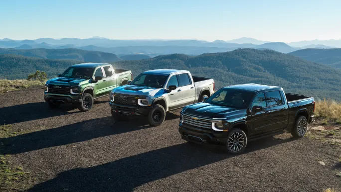 Three 2027 Chevrolet Silverado 1500 pickups parked on a mountain overlook, including Trail Boss, ZR2, and High Country models.