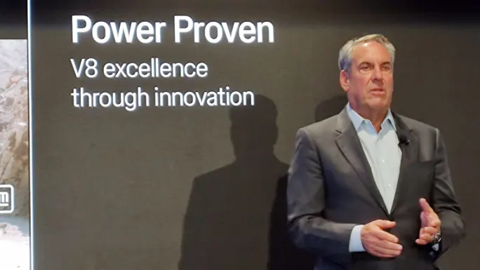GM executive speaks during a presentation beside a display reading “Power Proven: V8 excellence through innovation.”