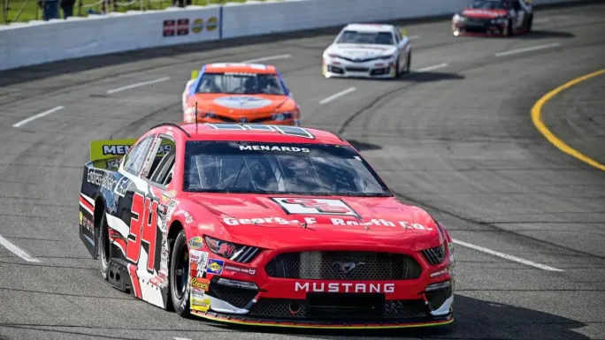 Red, black, and white No. 34 Ford Mustang leads several race cars around a paved racetrack during an ARCA Menards Series race.