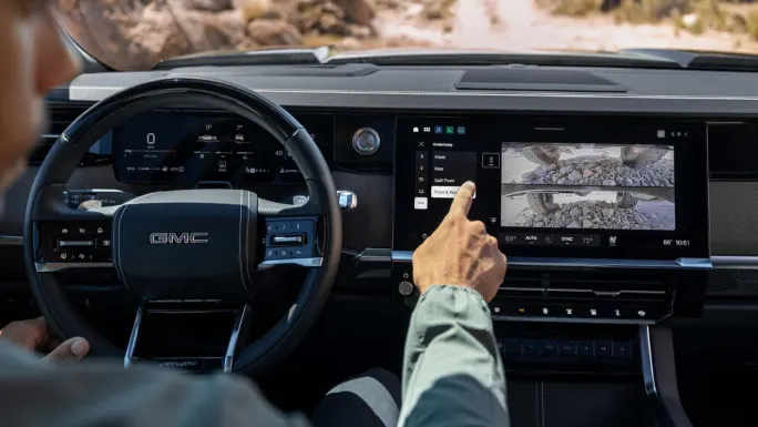 Driver uses the center touchscreen in a 2027 GMC Sierra 1500 AT4X to view front and rear underbody camera feeds while off-road.