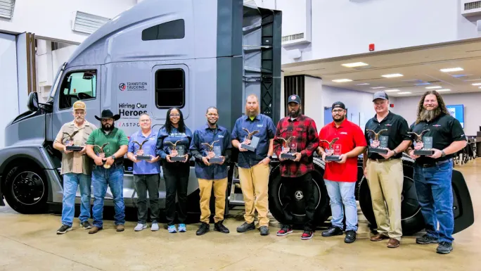 Group of Transition Trucking award semifinalists holding trophies in front of a branded semi-truck during an indoor event.