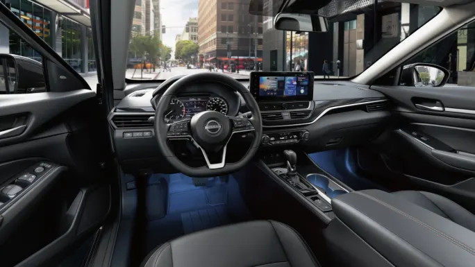Interior view of the 2027 Nissan Altima showing the steering wheel, dashboard, center touchscreen, front seats, and center console.