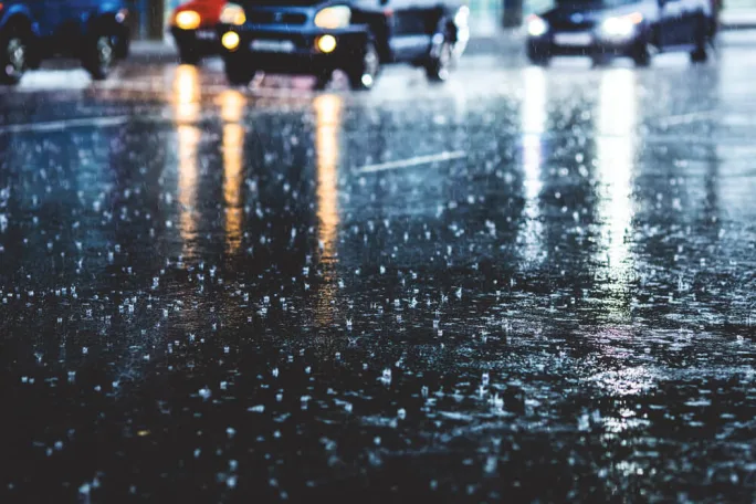 Cars driving through heavy nighttime rain on a reflective road surface depicting hazardous storm conditions that can lead to vehicle damage and insurance claims