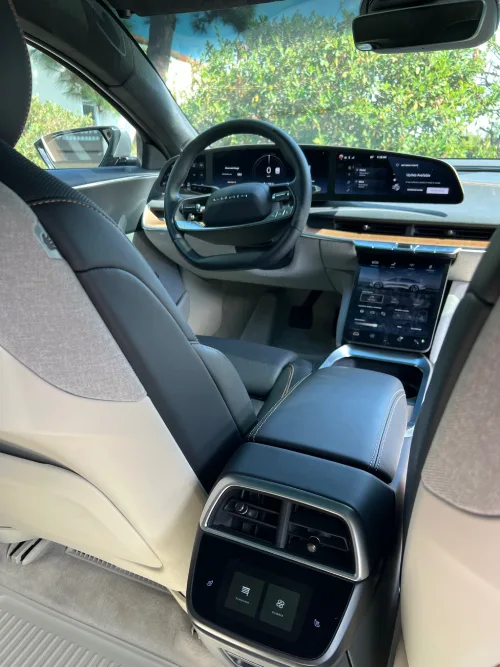 A view from the rear seat of the driver seat, steering wheel, and dashboard of a Lucid Air sedan.