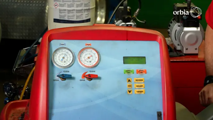 Close-up of an A/C recover, recycle, and recharge machine with low- and high-pressure gauges, a digital display, and service controls.