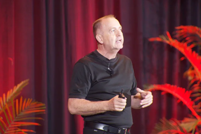Another shot of Richard Lowden on stage in front of a red curtain.