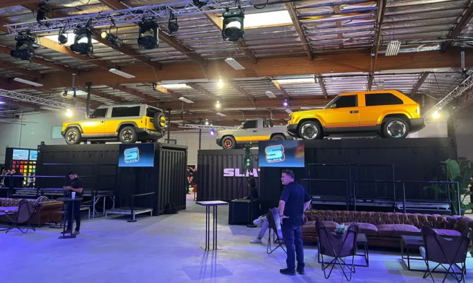 Three yellow-colored Slate models displayed on raised platforms ringed with black curtains.