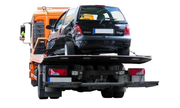 The rear view of a dented minivan on a flatbed tow truck.