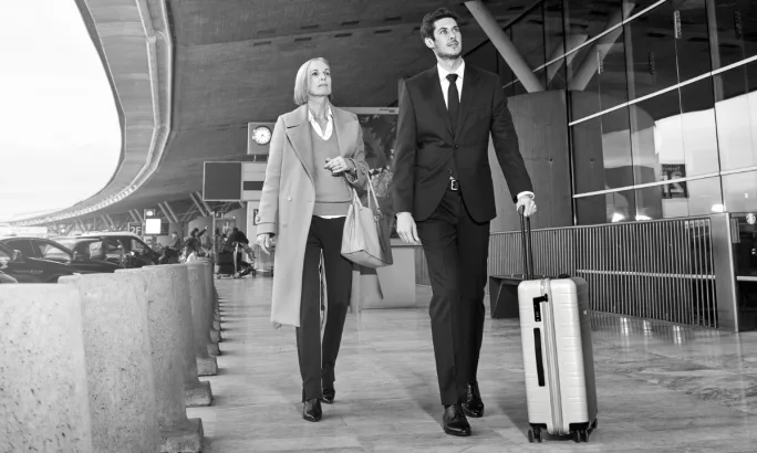 A chauffeur is walking with a client and rolling her suitcase on their way to a luxury sedan.