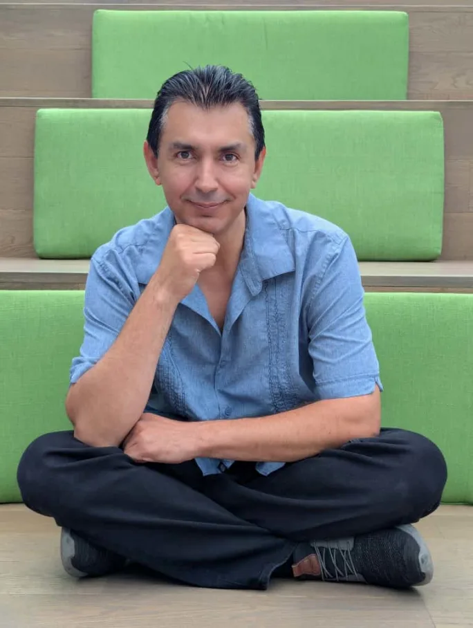 Carlos Bazan is sitting cross-legged in front of light green paneled steps.