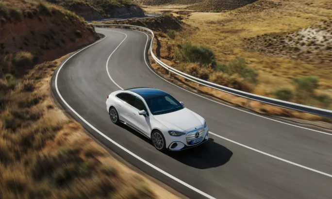 White Mercedes-Benz electric sedan driving on a winding road through dry hills, showcasing the 2027 C-Class EV in motion.