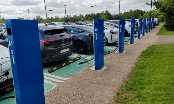 A back view of a row of electric vehicles lined up at parking lot chargers.