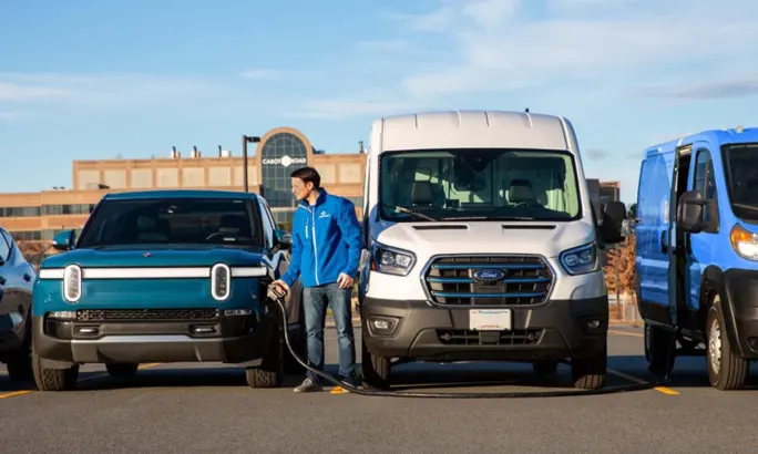 A fleet manager charges an EV in a row of electric fleet vehicles in a parking lot.