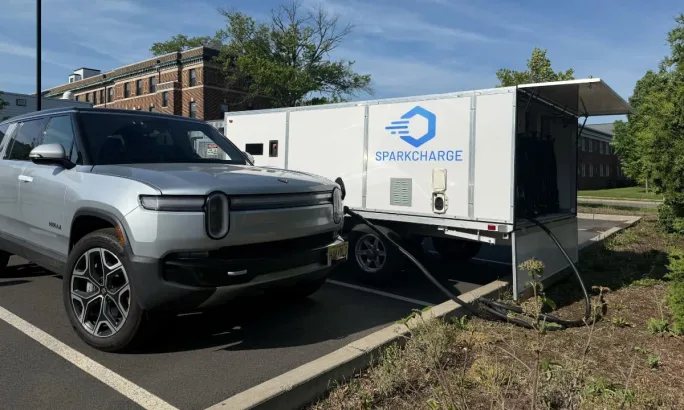 A Rivian SUV charging from a SparkCharge mobile rectangular charger.