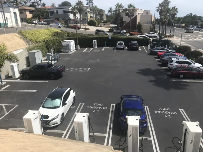 Overview photo of the finished charging depot in Encinitas, California, with chargers lined up on a smooth parking surface with a large generator situated in a far corner of the parking lot.