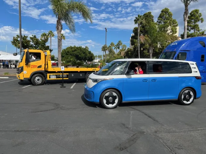 A flatbed truck, a semi, and a VW bus in a parking lot at a ride and drive event.