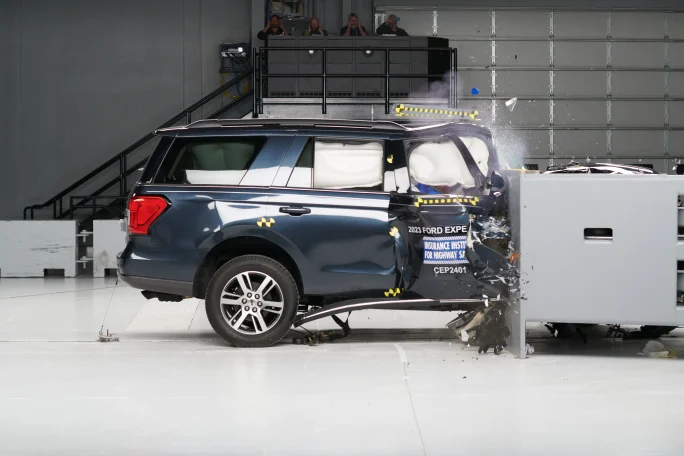 A dark blue Ford Expedition is shown with its front end entirely crumpled and air bags deployed in a crash testing facility.