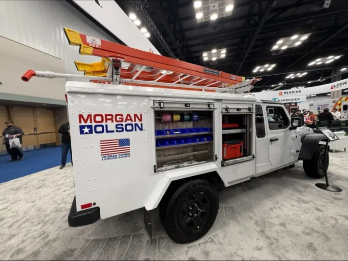 Side view of Morgan Olson Kestrel service truck with open storage compartments, ladder rack, and organized tool bins on display at NTEA Work Truck Week trade show.