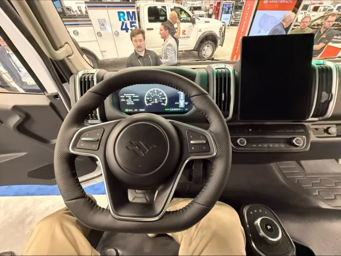 Interior driver’s view of Harbinger HC Series Cab electric medium-duty work truck at Work Truck Week, showing steering wheel, digital gauge cluster, large center display, and cab-forward layout.