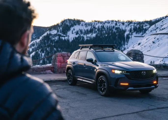 A blue Mazda SUV parked at an overlook of snowy mountains.