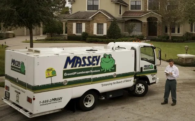  Massey Services pest control truck parked in a residential neighborhood with an employee standing beside it.