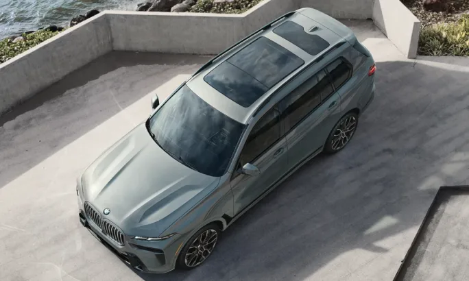 An aerial view of a mint green 2025 BMW X7 on gray pavement.