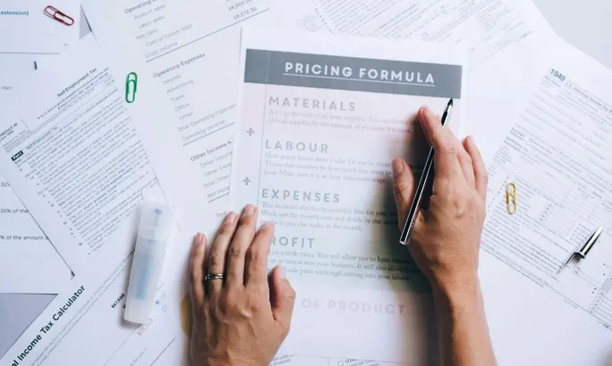 Human hands working on a spread of work papers on a desk focused on pricing.